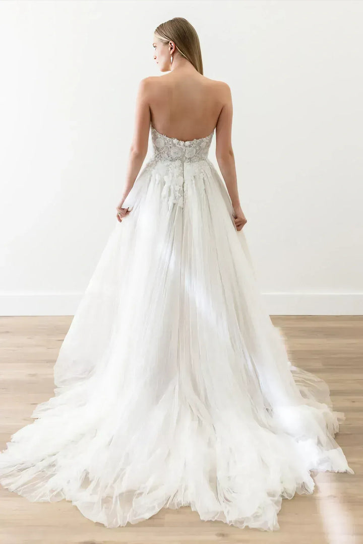 Woman wearing a white wedding dress with a flowing train on a wooden floor.