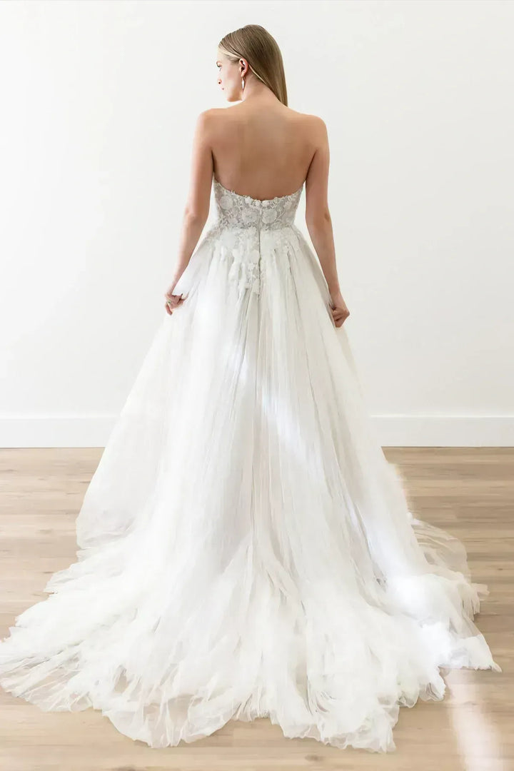 Woman wearing a white wedding dress with a flowing train on a wooden floor.