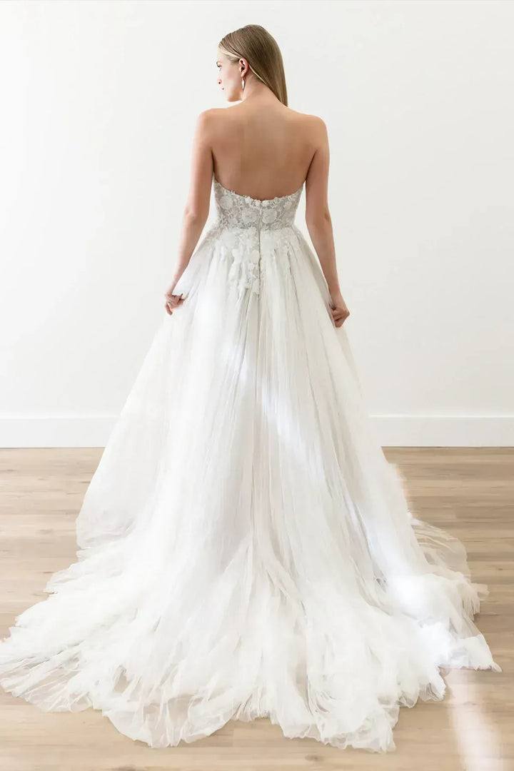 Woman wearing a white wedding dress with a flowing train on a wooden floor.
