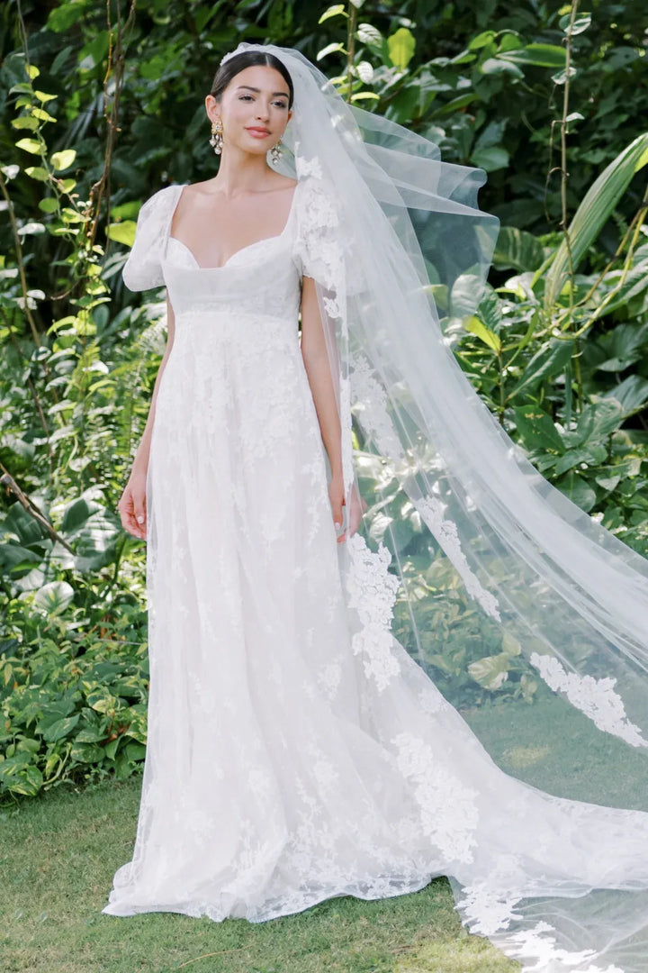 Woman in a white wedding dress with a long veil standing in a garden.