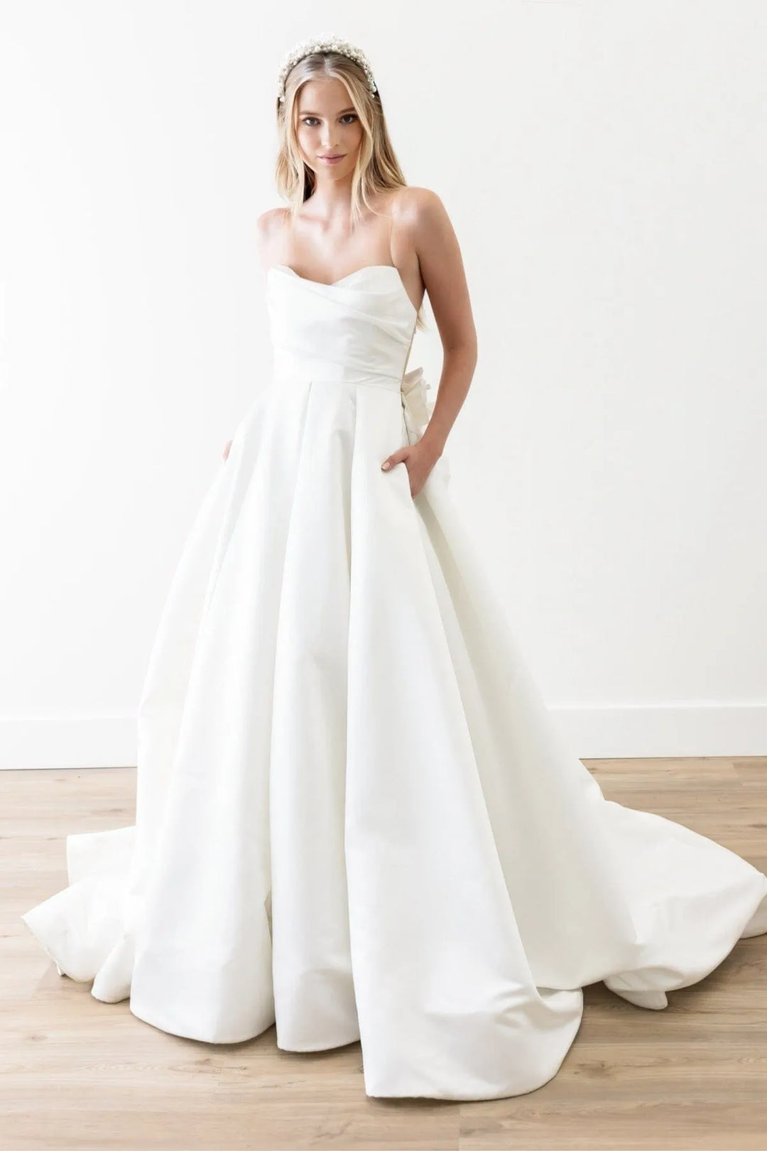 Woman wearing a white strapless wedding dress on a plain background