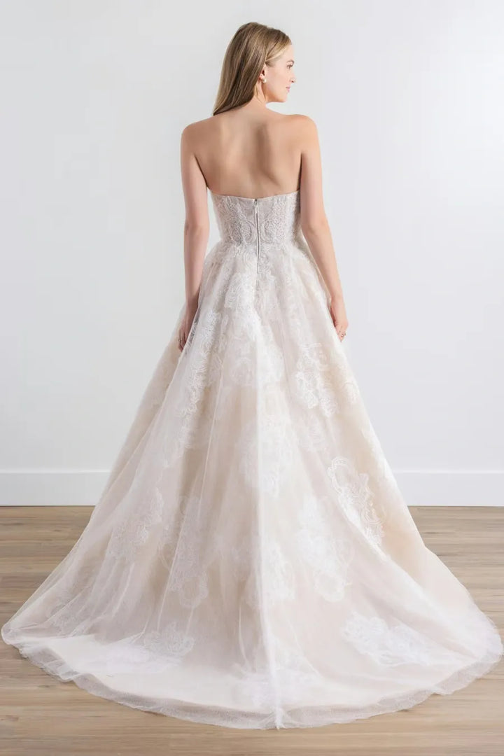 Woman wearing a strapless wedding dress with a flowing skirt on a plain background