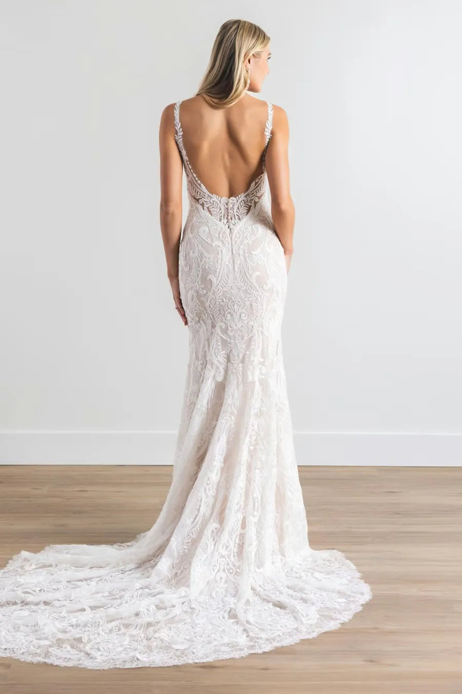 Woman wearing a white lace wedding dress with a long train on a plain background