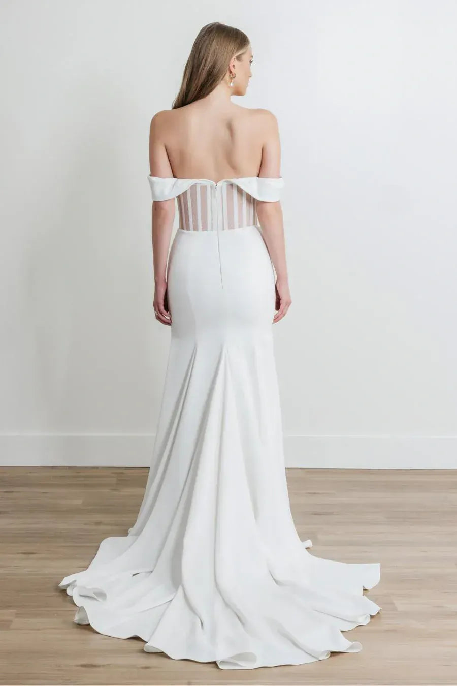 White off-shoulder wedding dress with sheer back on a plain background