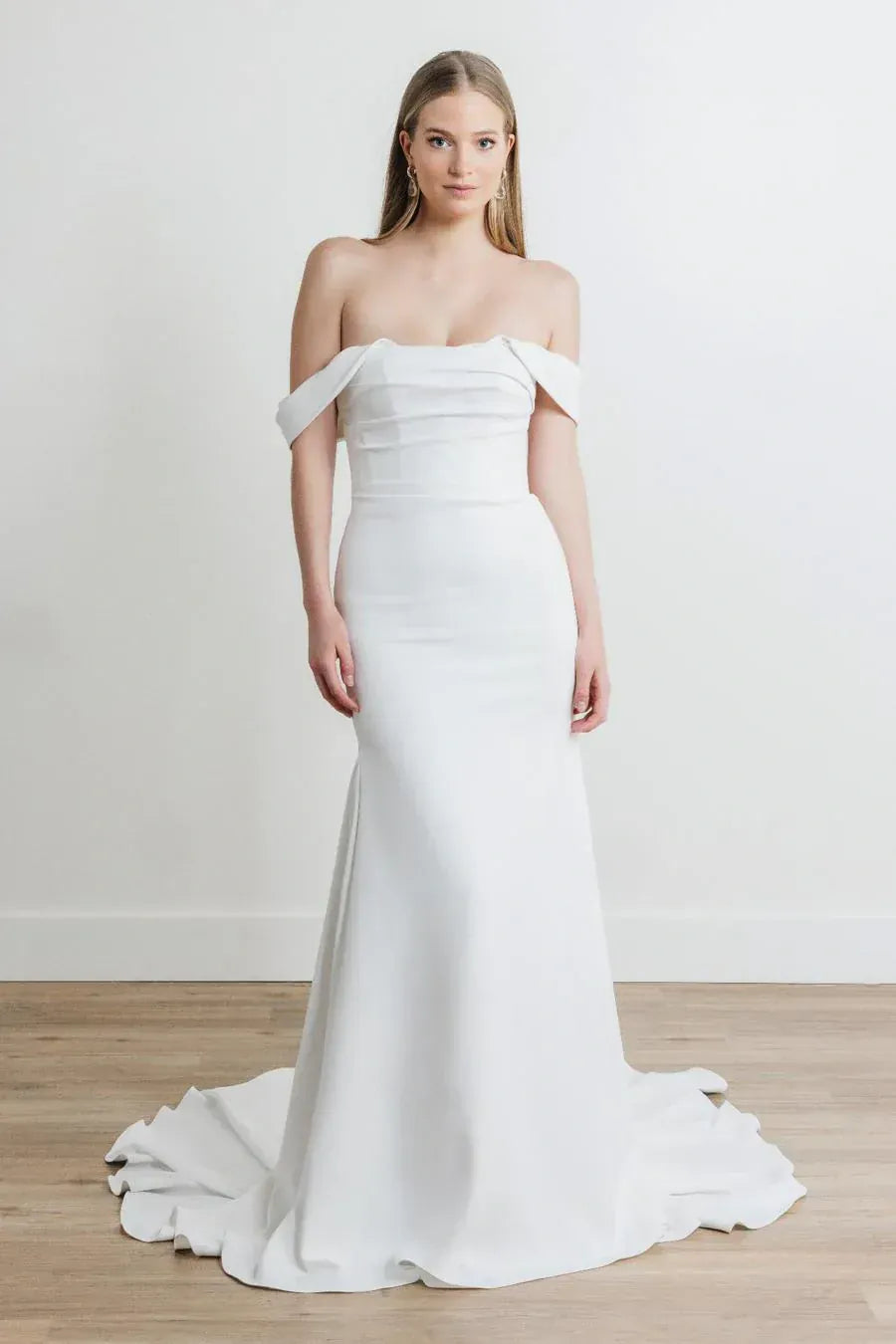 Woman wearing a white off-shoulder wedding dress on a plain background