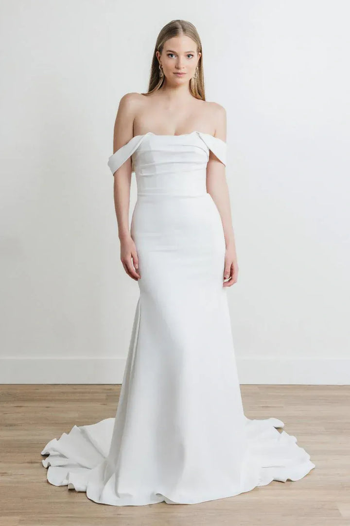 Woman wearing a white off-shoulder wedding dress on a plain background