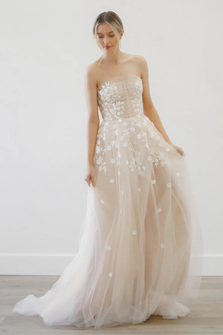 Woman wearing a strapless wedding dress with floral details on a white background