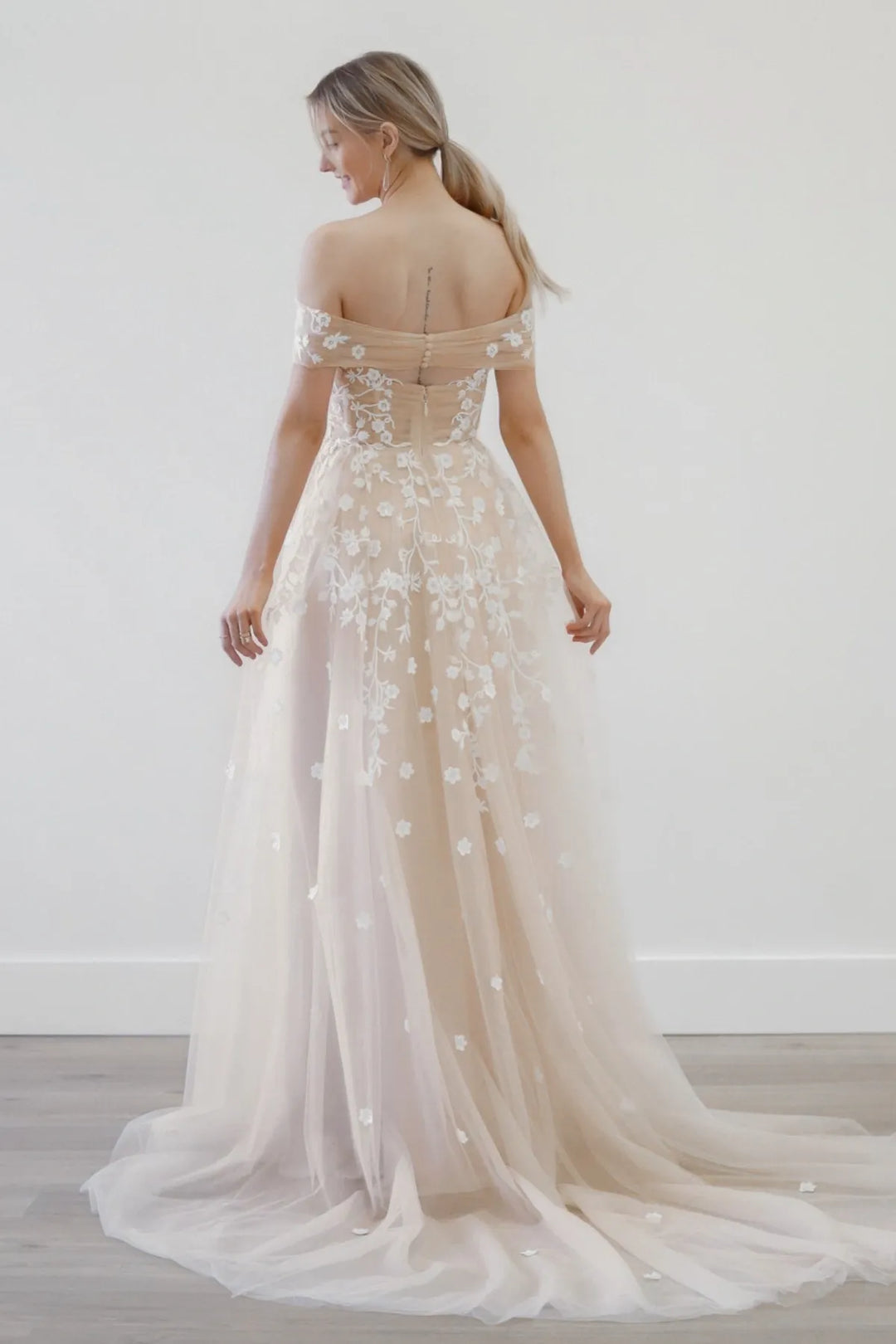 Woman wearing a flowing wedding dress with floral details against a white background