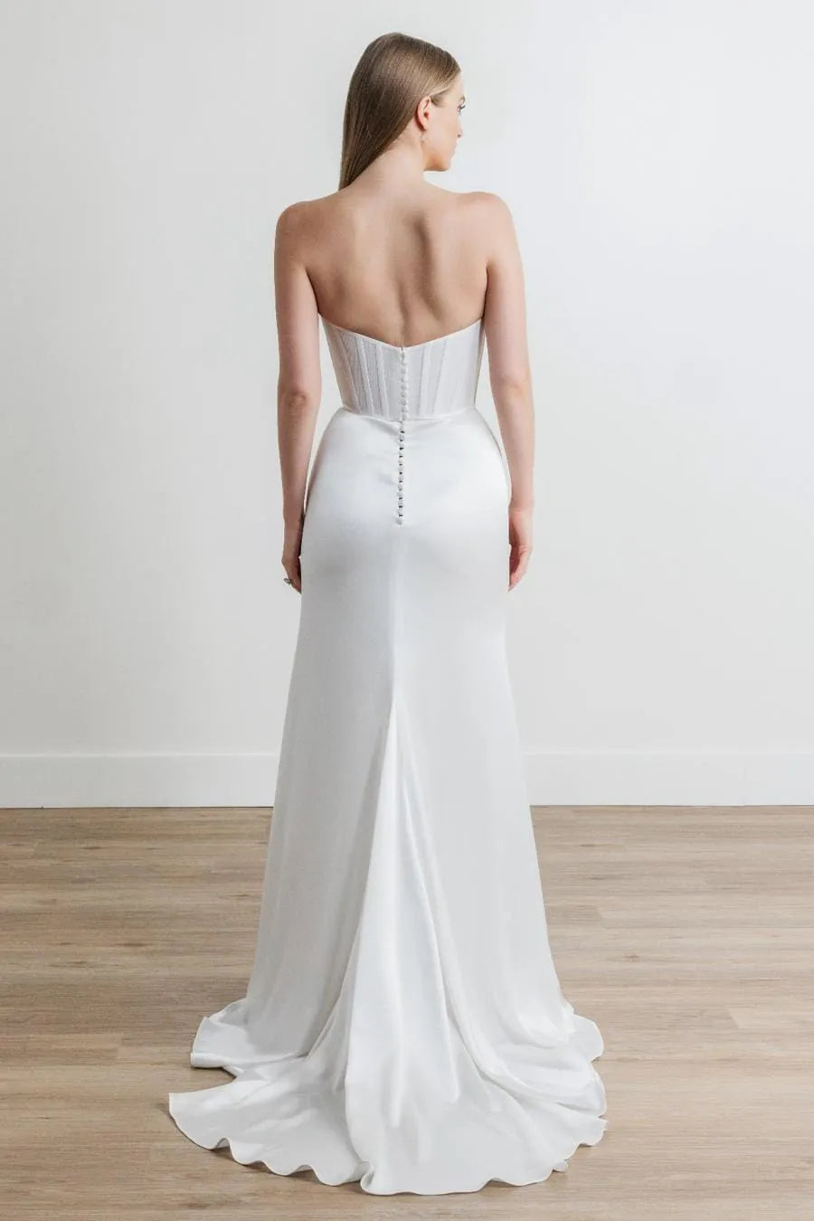 Woman wearing a strapless white wedding gown on a plain background