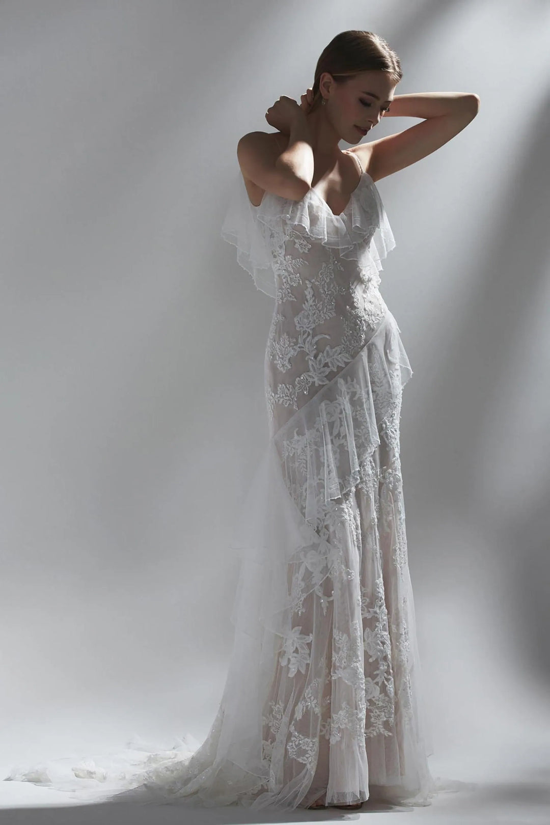 front of watters nephele blush lace fitted wedding dress with a v neckline and ruffled tulle accents on the bodice and skirt
