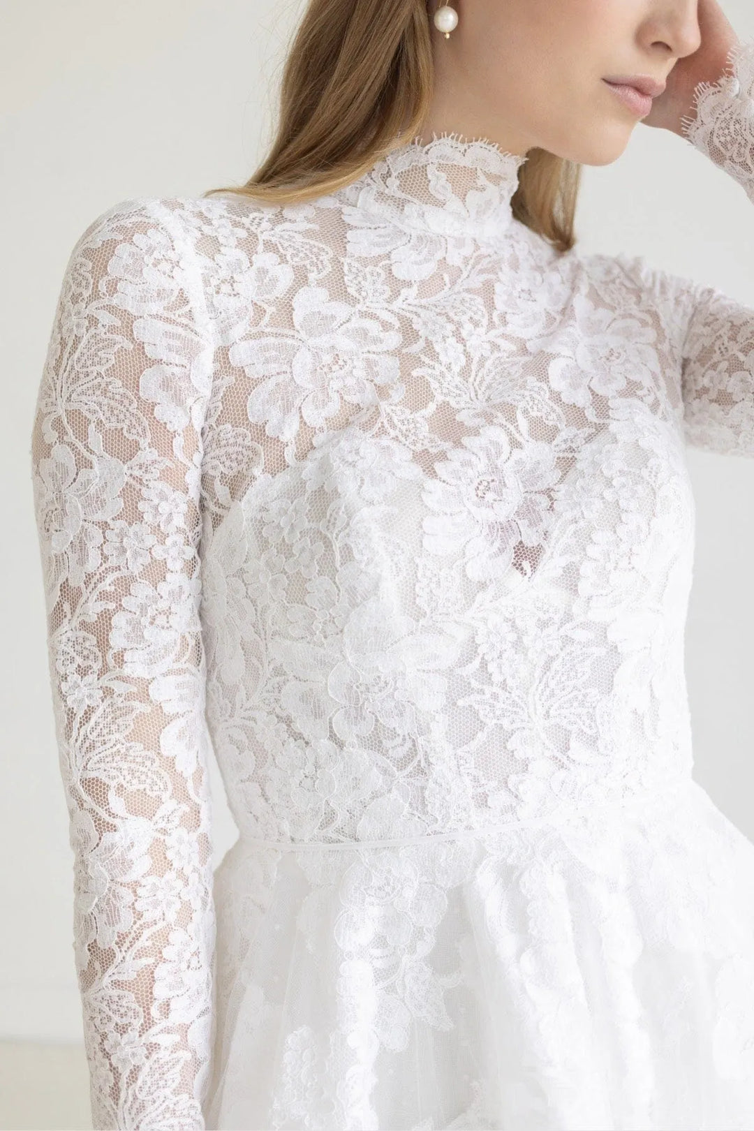 Close-up of a white lace dress with long sleeves on a plain background