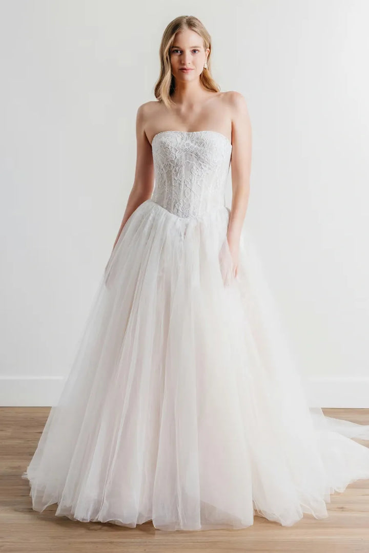 Woman wearing a strapless wedding dress with intricate lace detailing on a plain background
