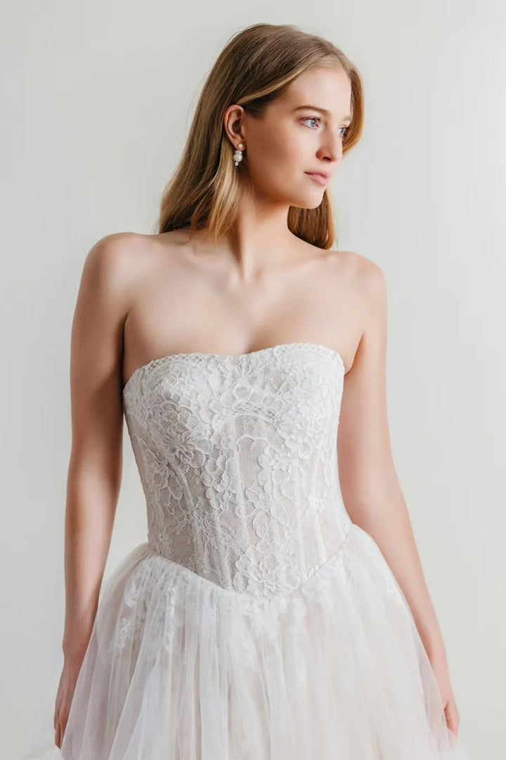 Woman wearing a strapless lace wedding dress against a plain background