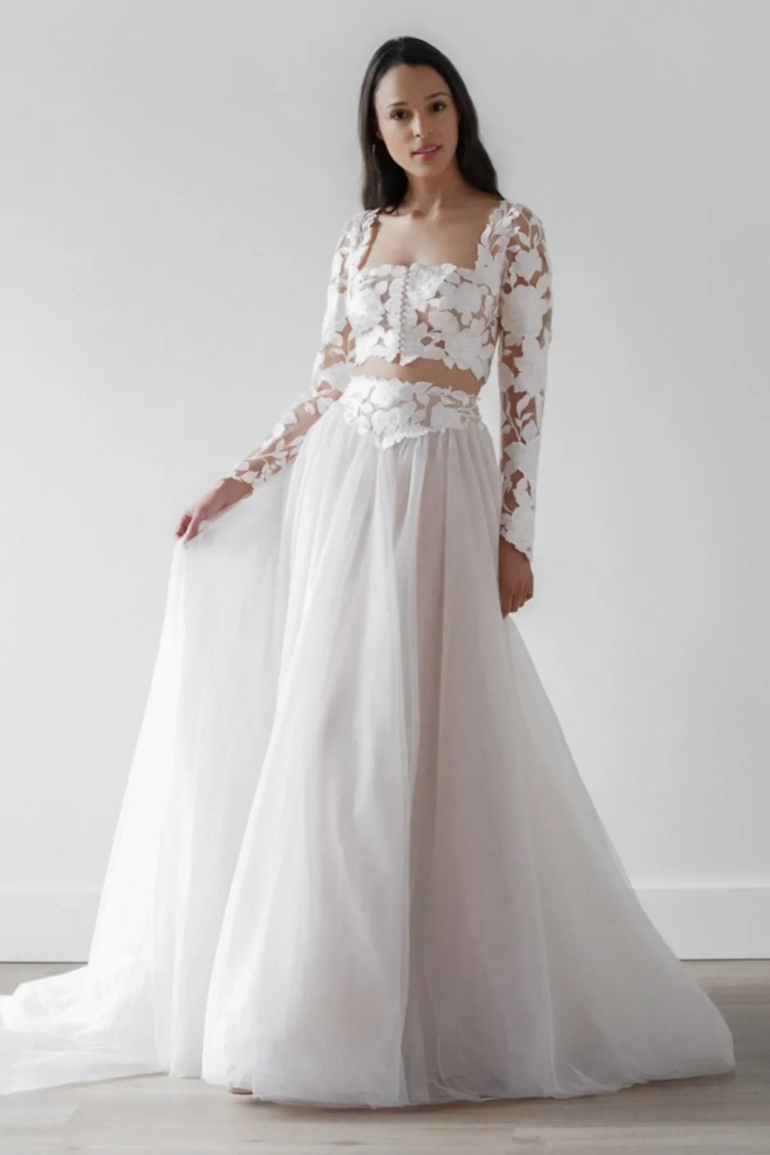 Woman wearing a white lace wedding dress against a plain background