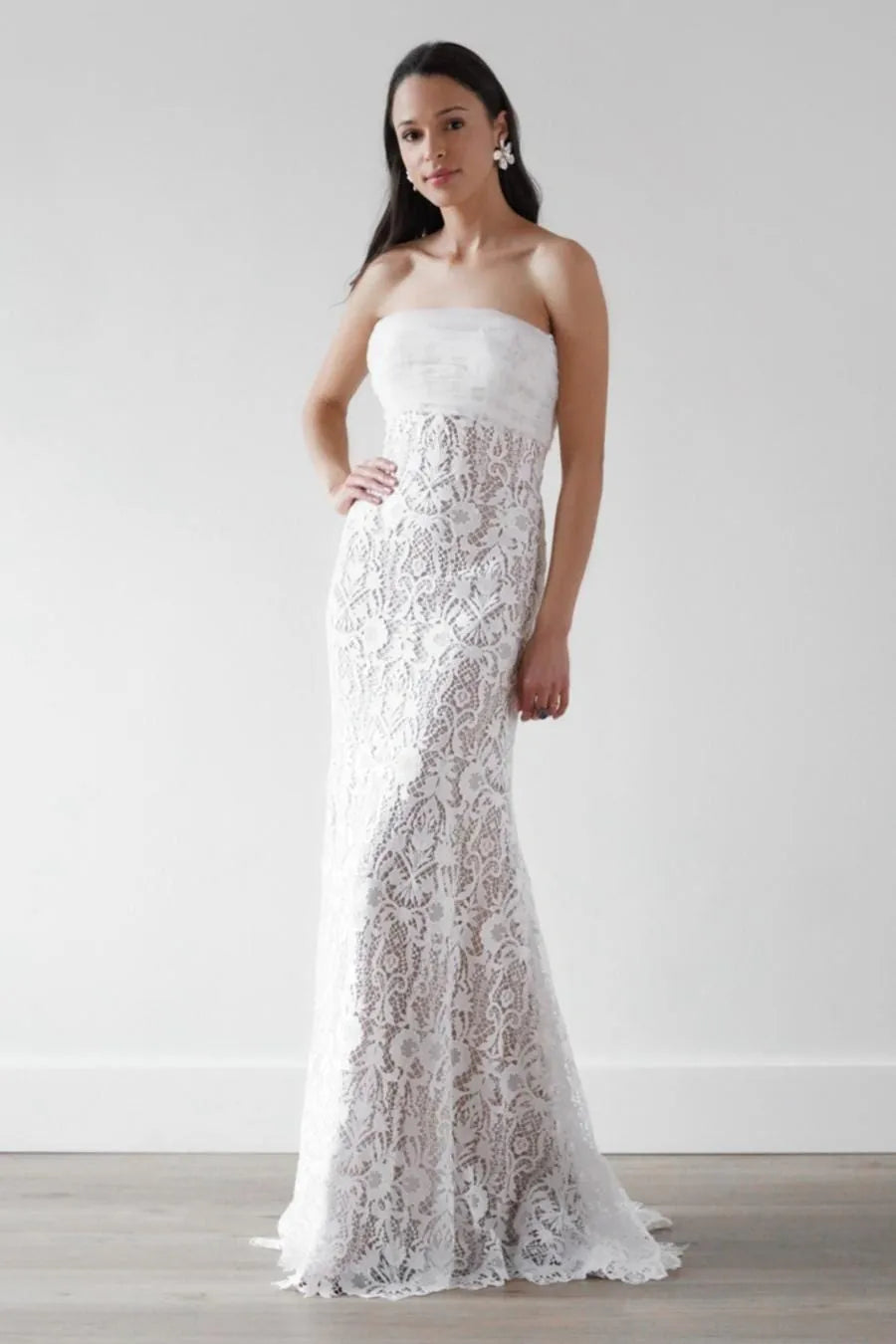 Woman wearing a strapless lace wedding dress against a plain background