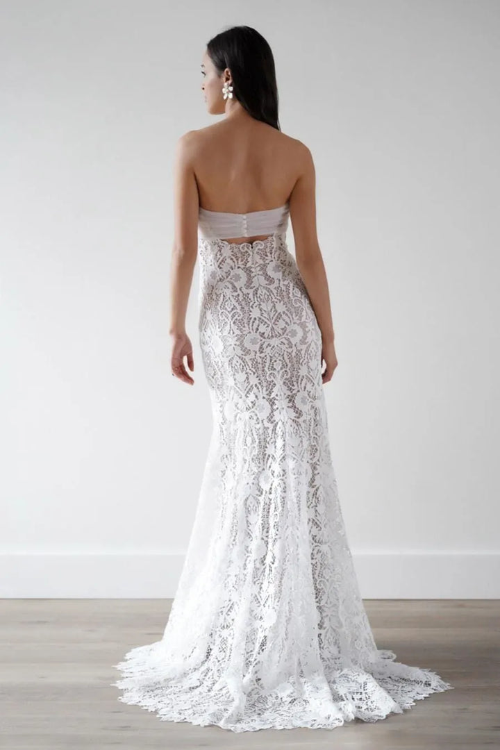 Woman wearing a strapless lace wedding dress against a plain background