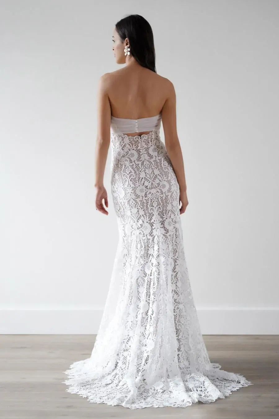 Woman wearing a strapless lace wedding dress against a plain background