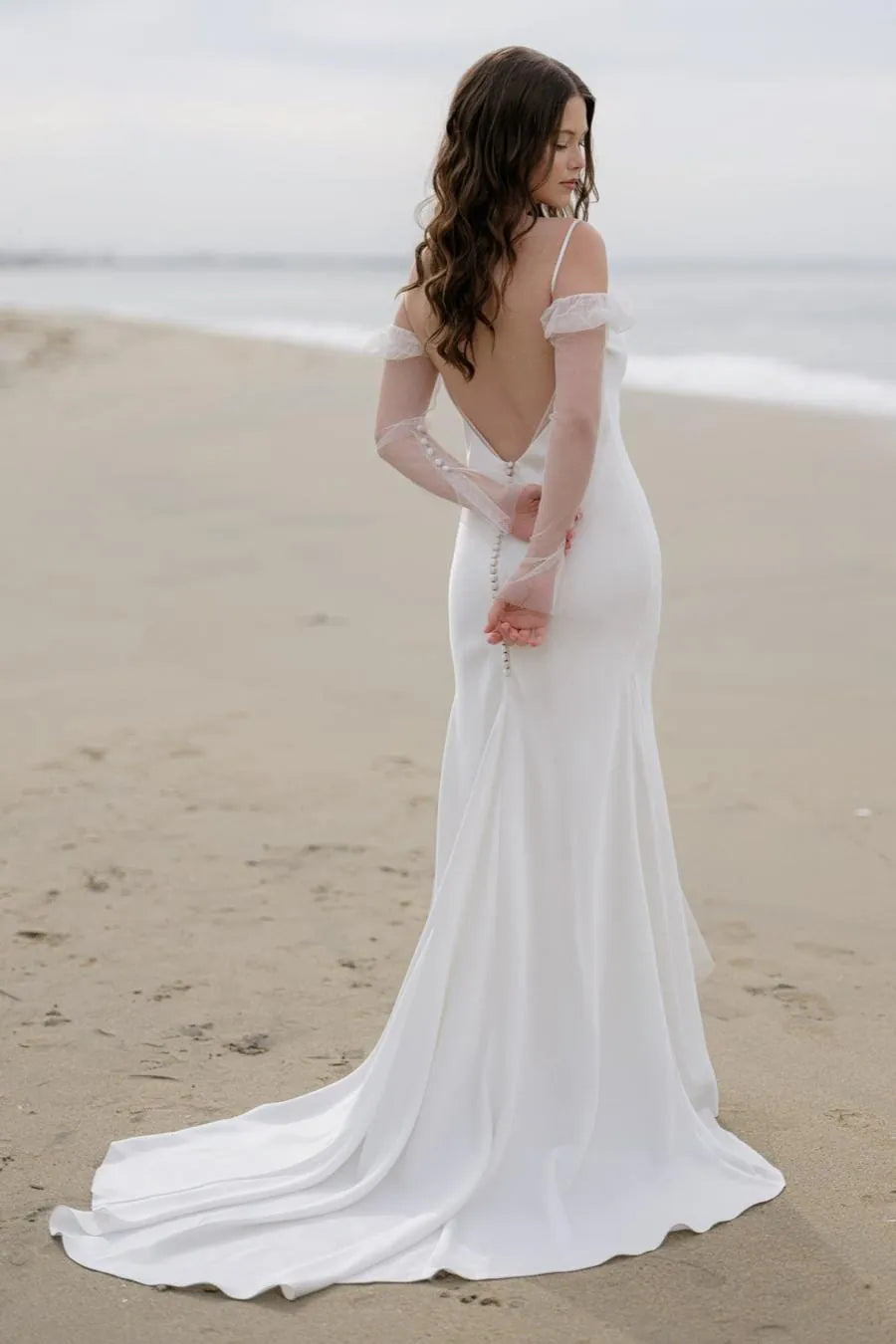 Woman in a white wedding dress standing on a beach.