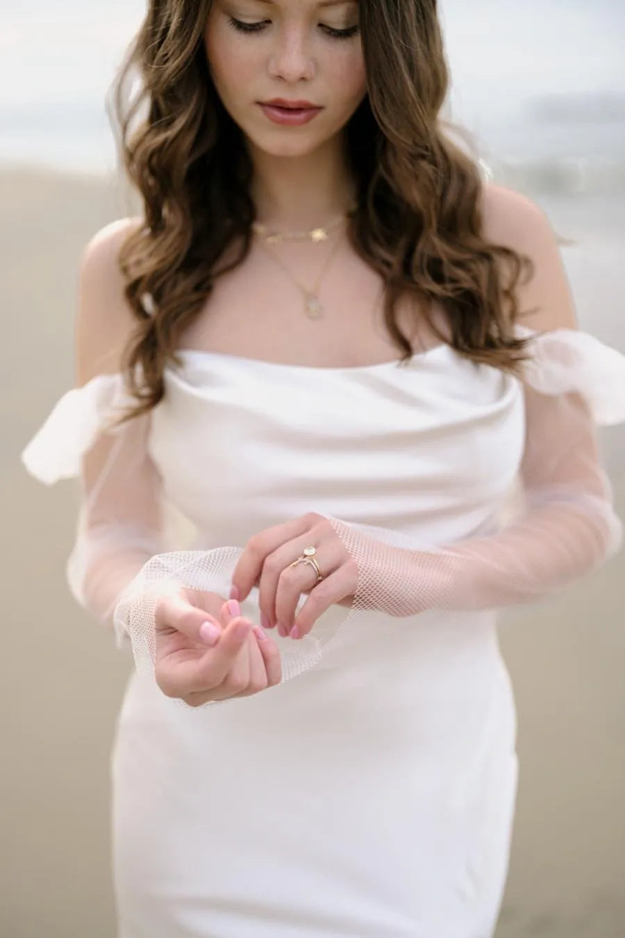 Woman wearing a white dress with sheer sleeves against a neutral background