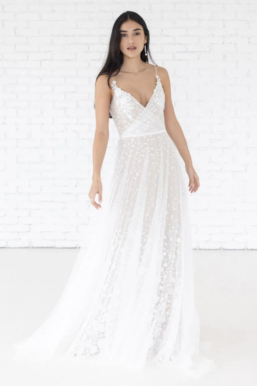 Woman wearing a white lace dress against a white brick wall.