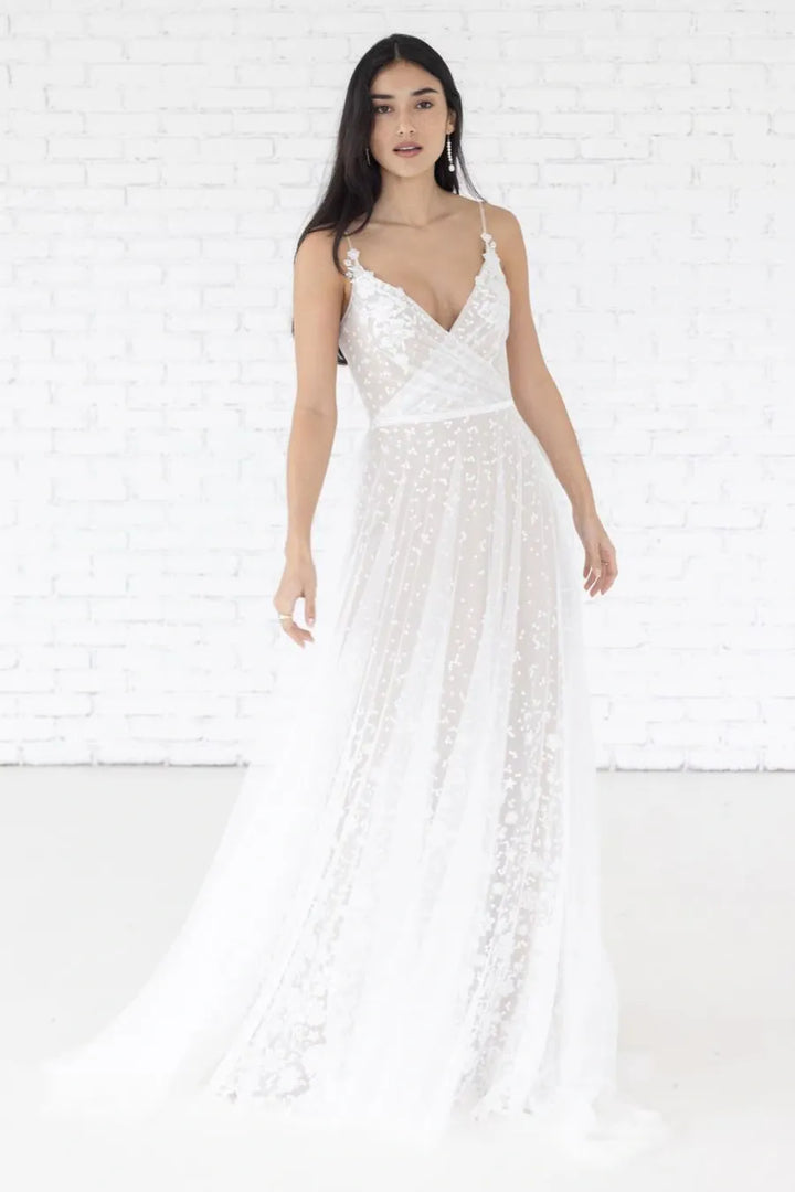 Woman wearing a white lace dress against a white brick wall.