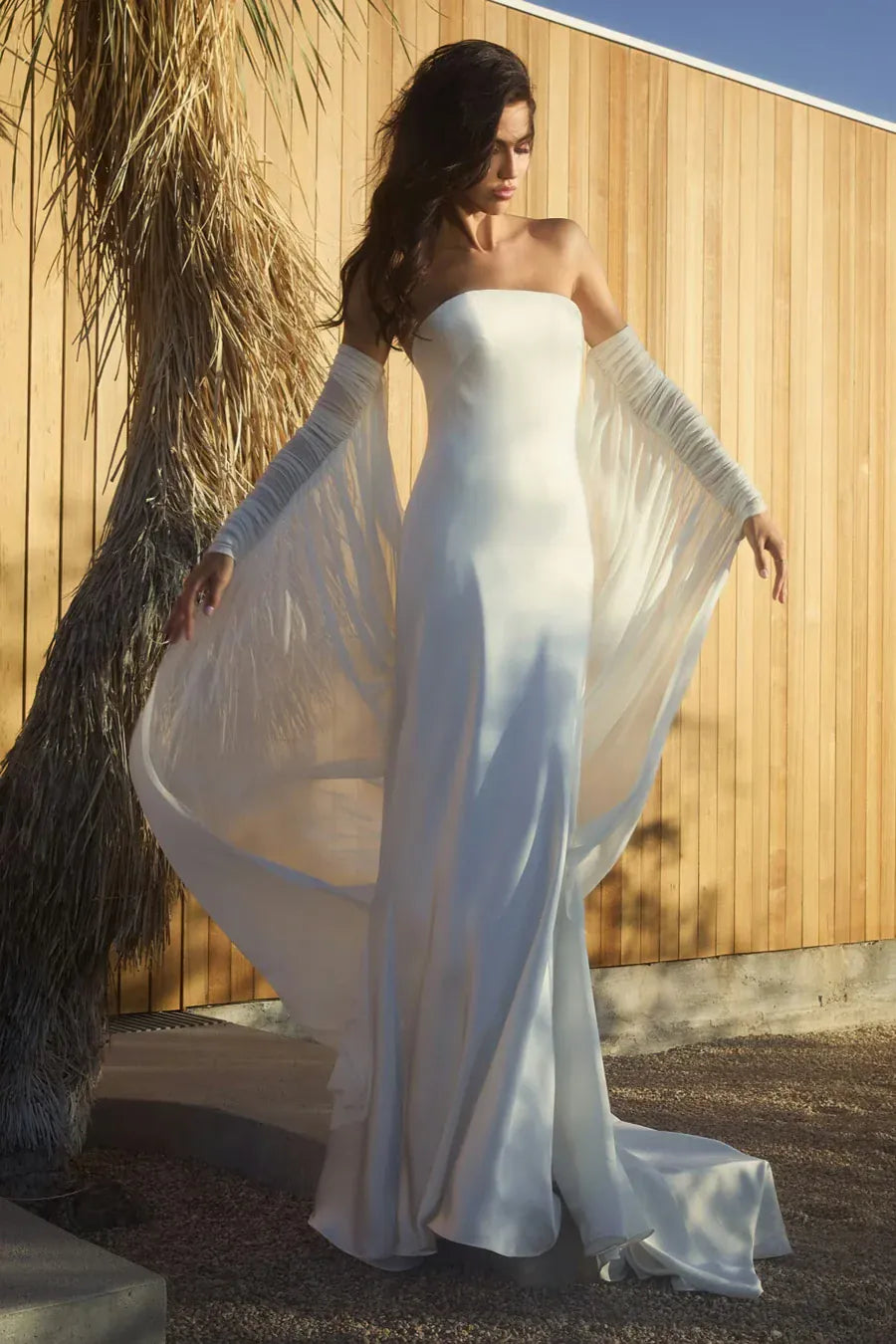 Woman in a white strapless gown with a long train standing against a wooden wall.