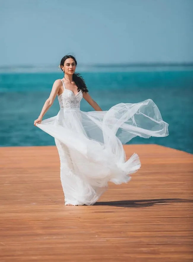 Woman in a white dress standing on a wooden platform with ocean and sky in the background