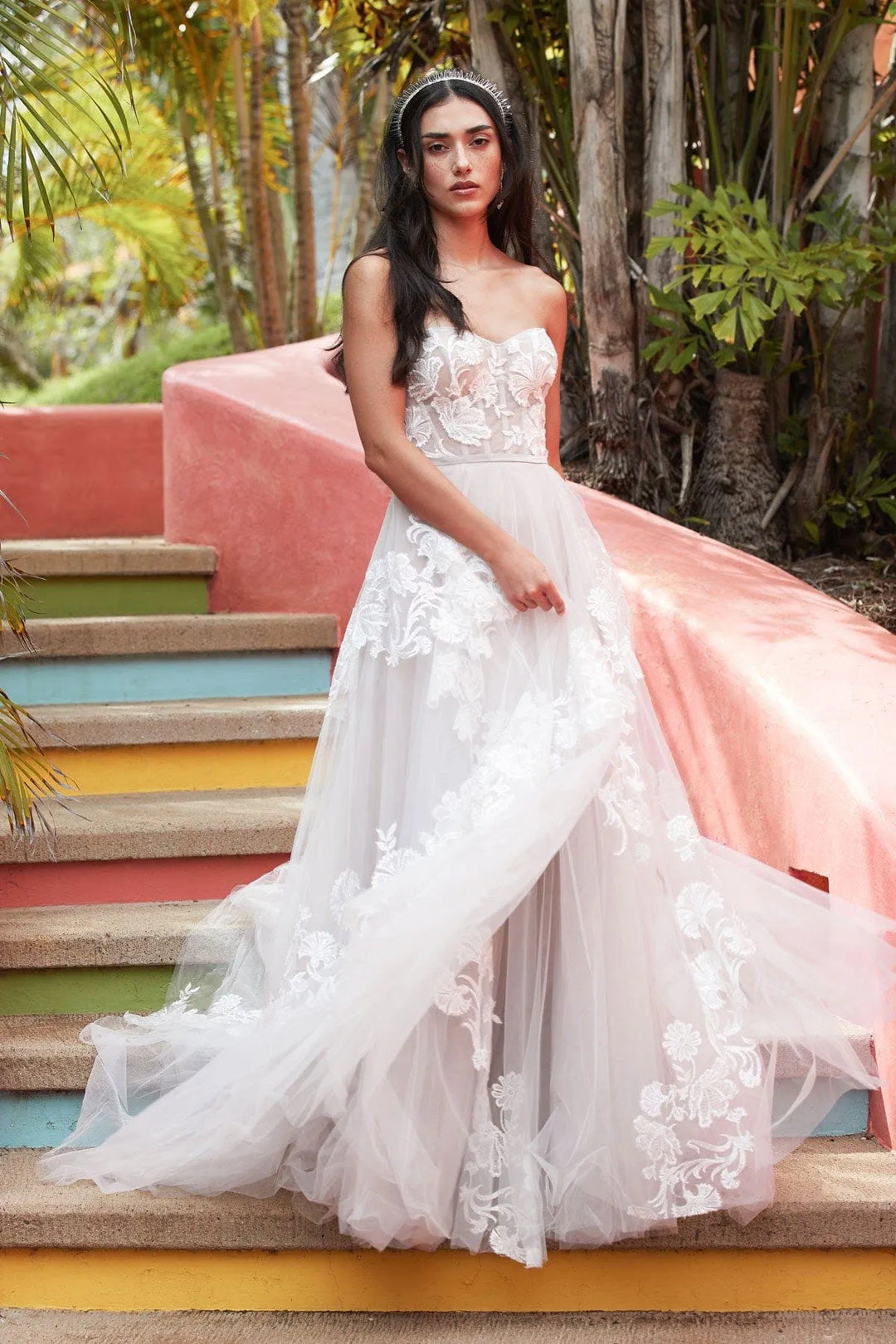 Woman in a white wedding dress standing on colorful steps with a tropical background