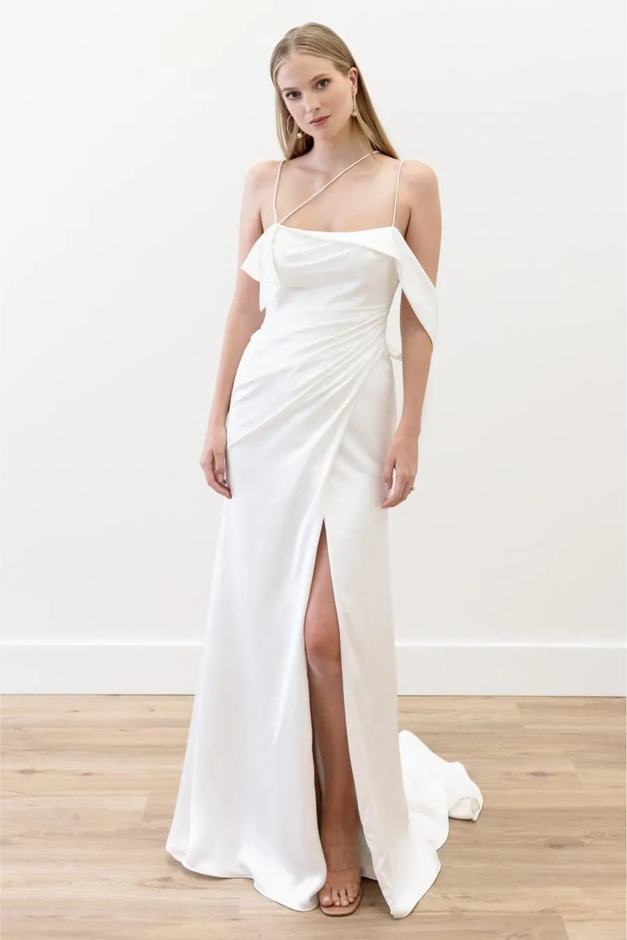 Woman wearing a white evening gown with a high slit on a plain background
