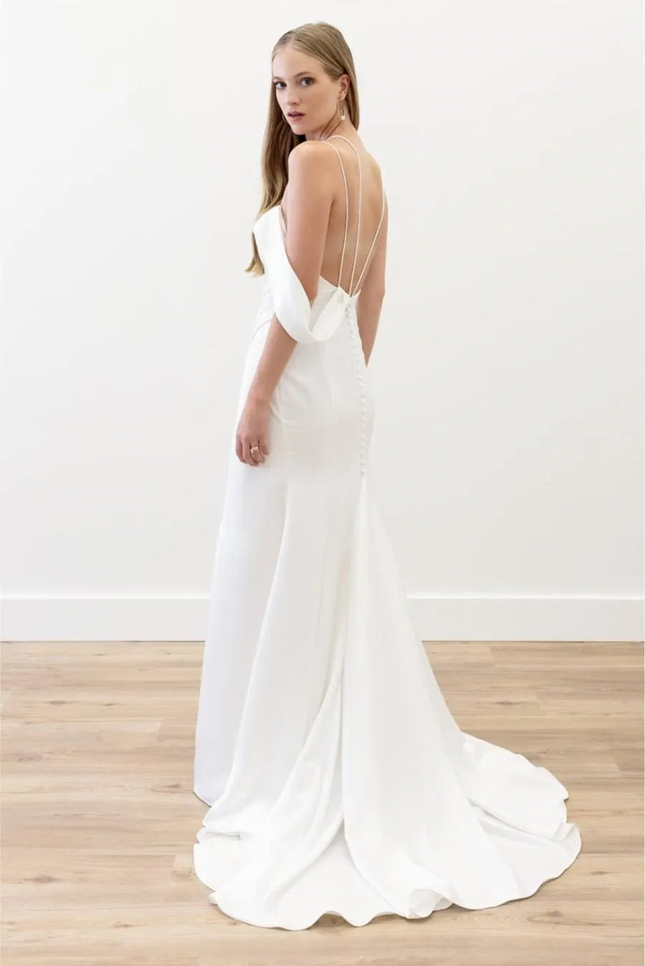 Woman wearing a white wedding dress with a sheer back on a wooden floor.