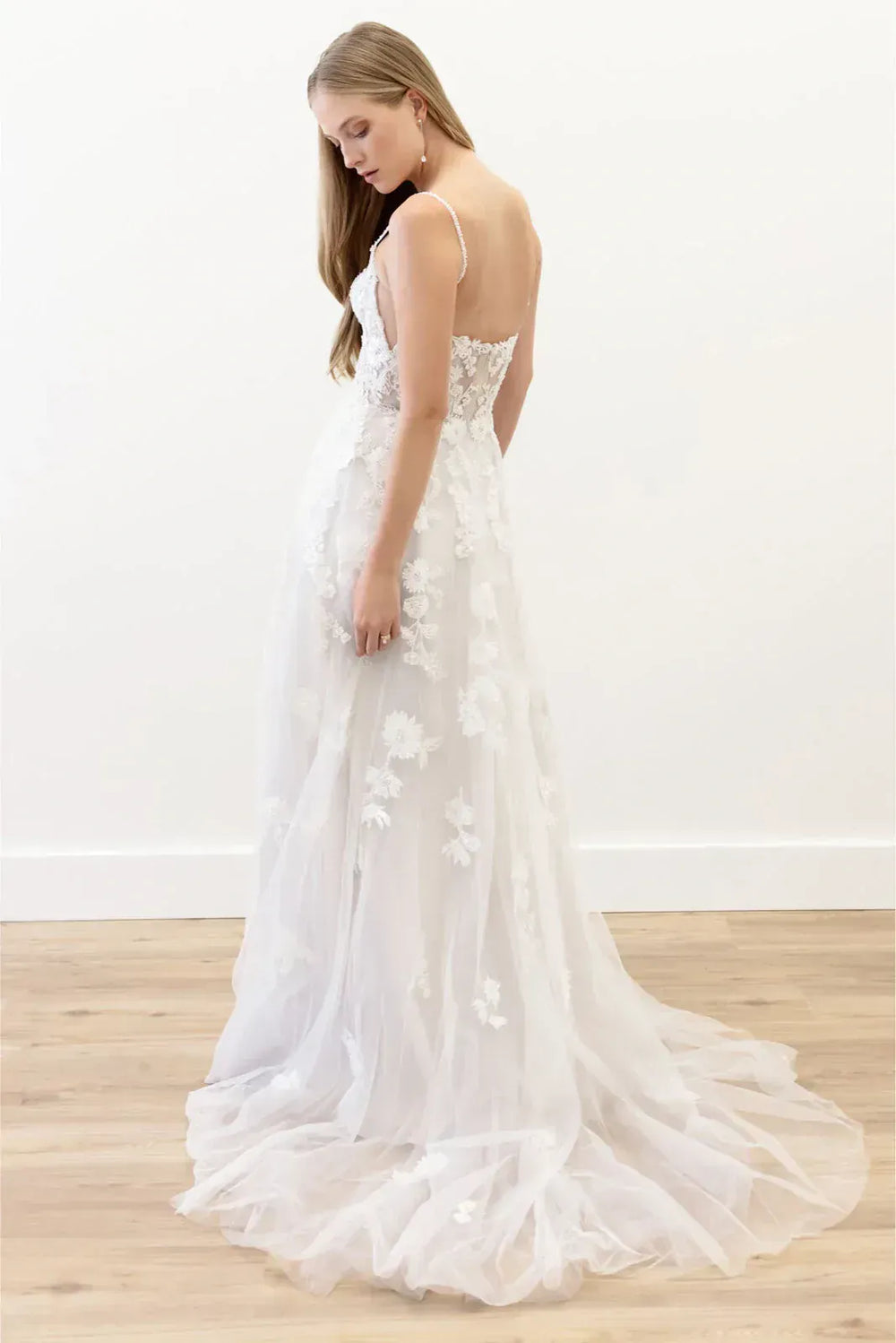 Woman wearing a white lace wedding dress on a wooden floor with a white background