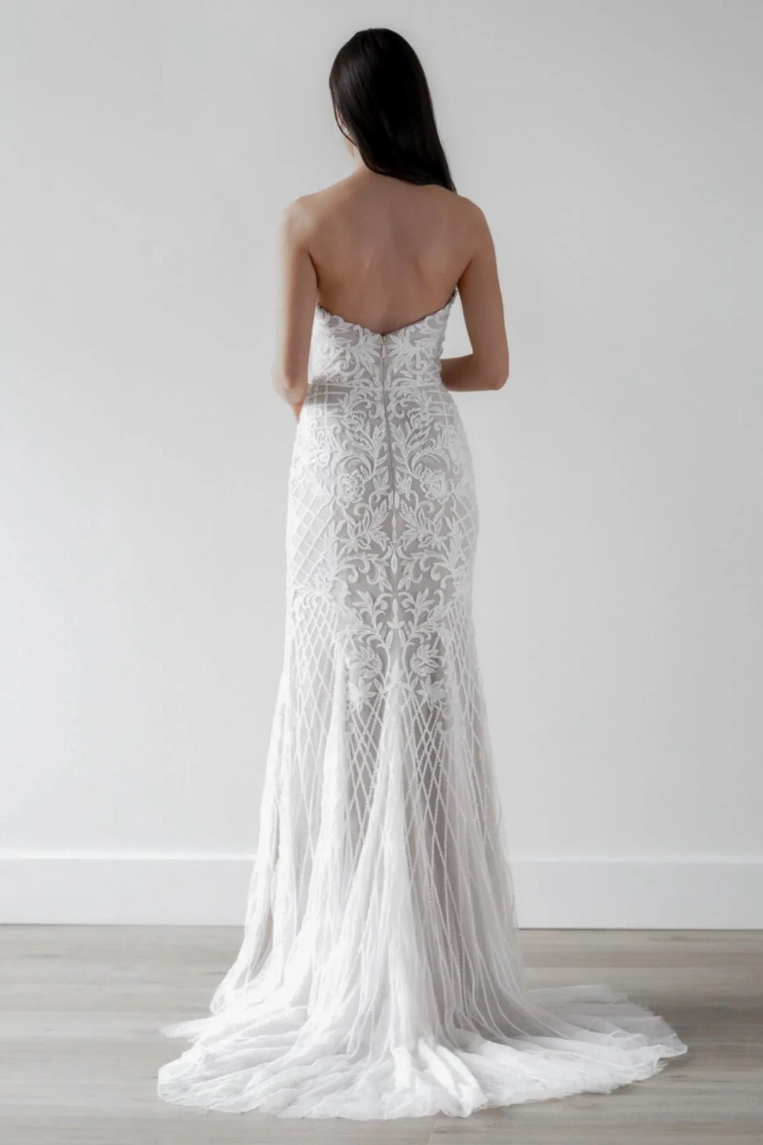 Woman wearing a strapless lace wedding dress with a plain white background