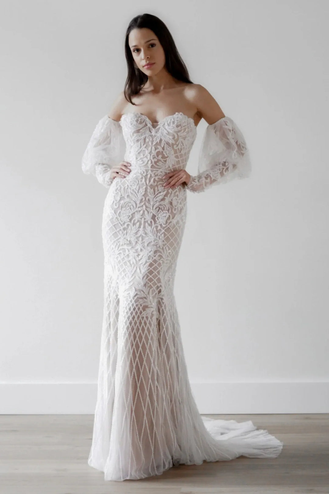 Woman wearing a white lace wedding dress with long sleeves against a plain background