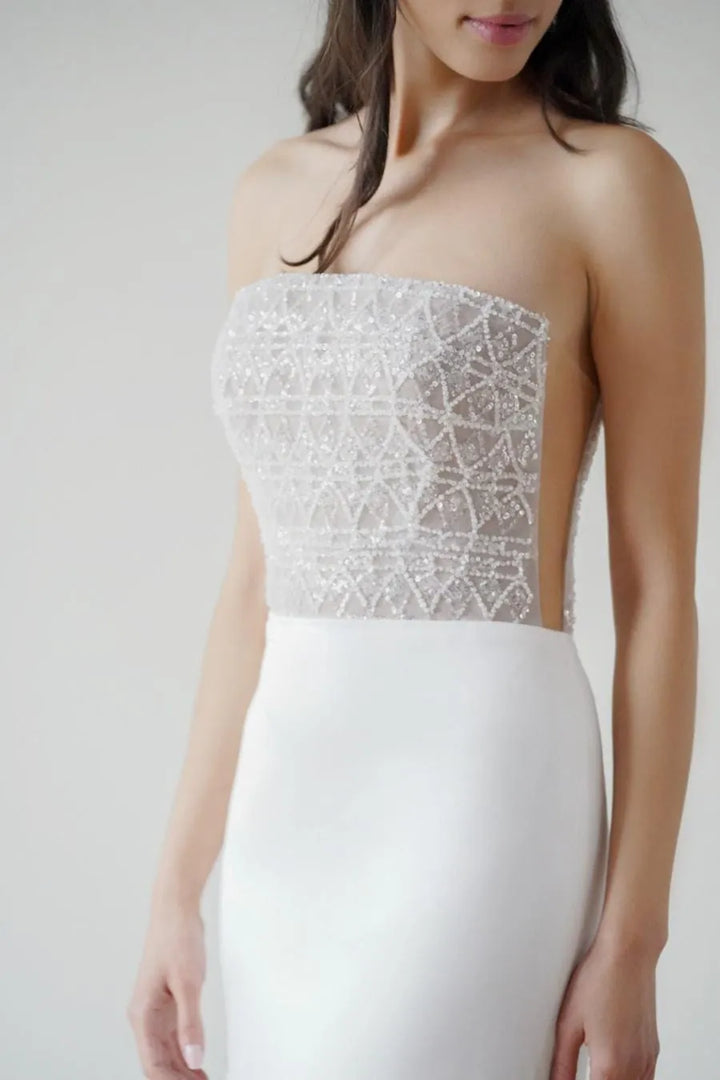 White strapless dress with intricate silver top on a plain background