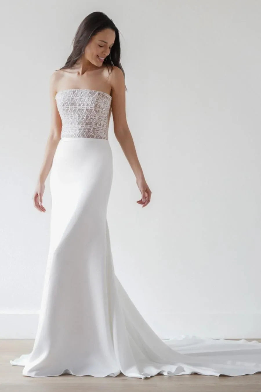 Woman wearing a strapless white wedding gown with lace top against a plain background
