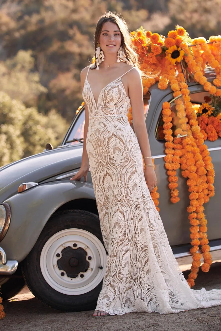 Woman in a white lace dress standing next to a vintage car decorated with orange flowers.