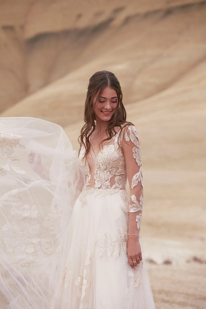 Woman in a white lace wedding dress standing in sand dunes