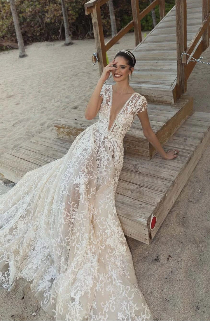 Woman in a lace wedding dress sitting on wooden steps by the beach