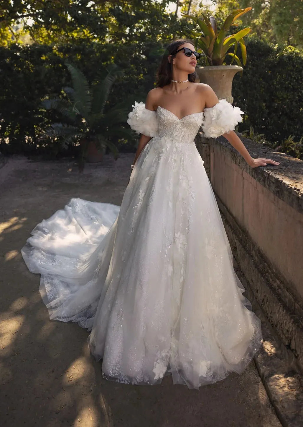 Woman in a white wedding dress standing outdoors with greenery in the background