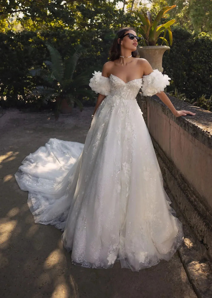 Woman in a white wedding dress standing outdoors with greenery in the background