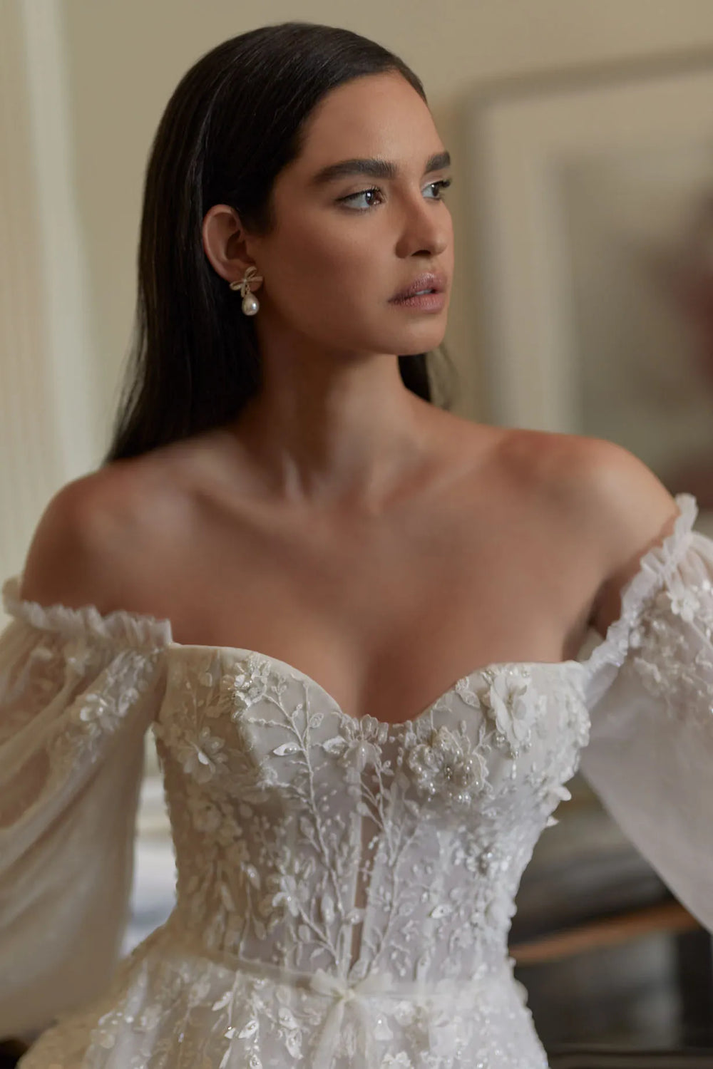 Woman wearing a white off-shoulder dress with intricate detailing.