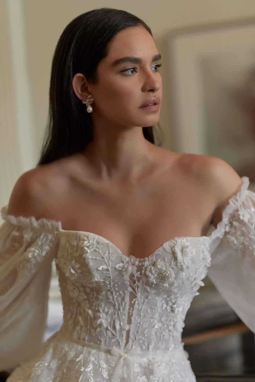 Woman wearing a white off-shoulder dress with intricate detailing.
