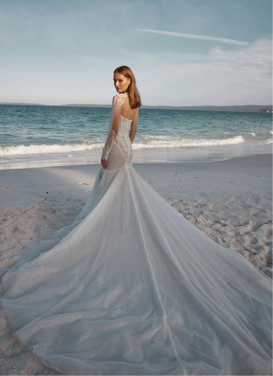 Woman in a light blue wedding dress standing on a beach with ocean in the background