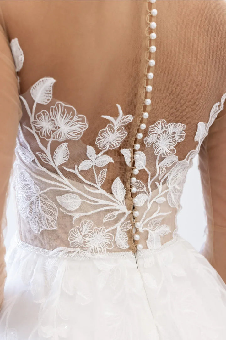 Close up of Locket by Watters Esme ivory tulle A-Line gown with illusion floral bodice and pearl buttons