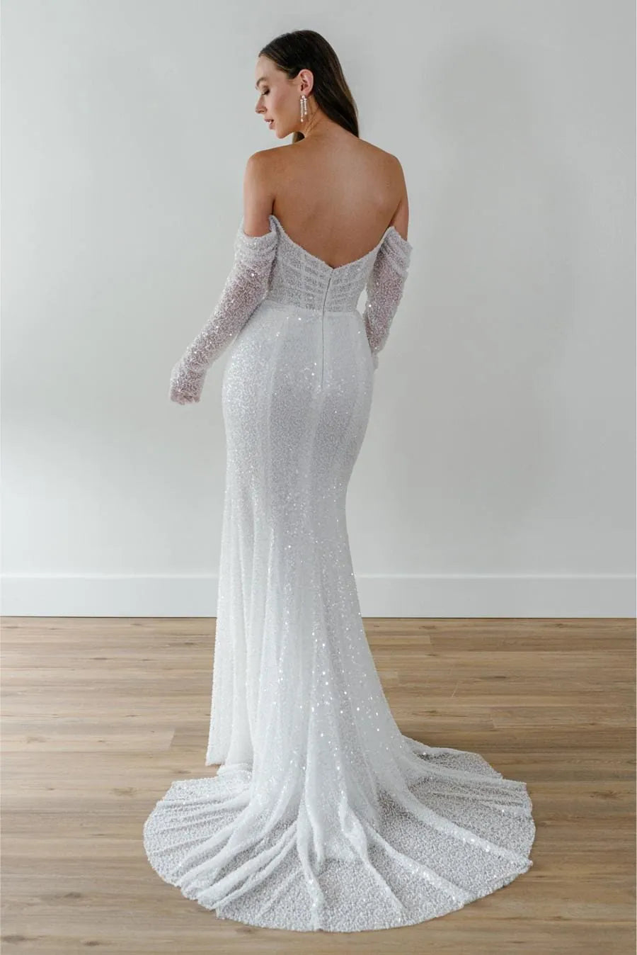 Woman wearing a sparkling silver wedding dress with long sleeves on a plain background