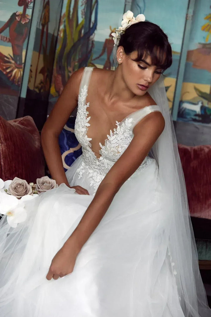 Woman in a white wedding dress with a long veil, sitting on a couch with floral decorations.